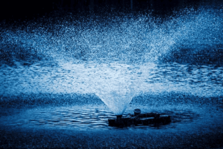 A blue fountain spraying water in a pond with an aerator.