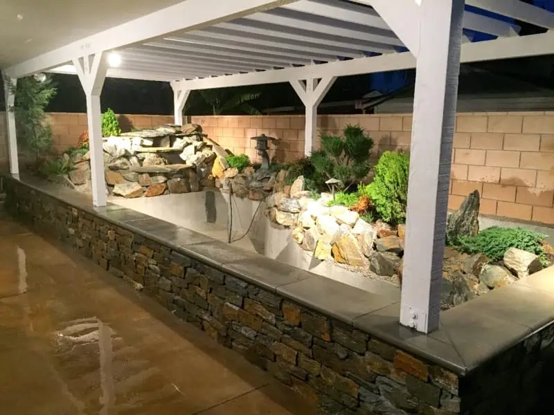 A stone patio with a water feature and plants, requiring minimal maintenance and occasional repair.