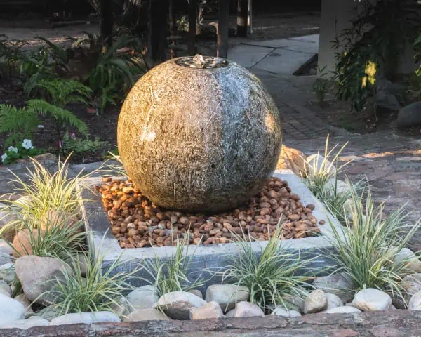 A large stone water fountain in a garden, offering services for the management of the lake.