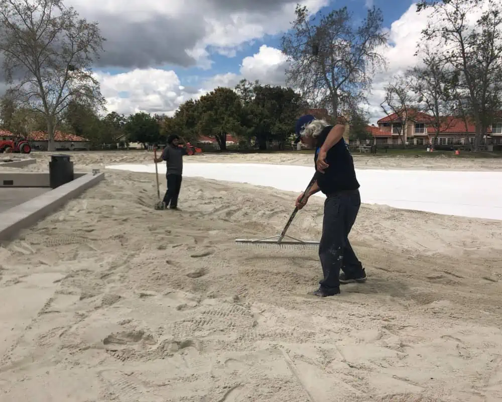 Two men working on the sand in a park.