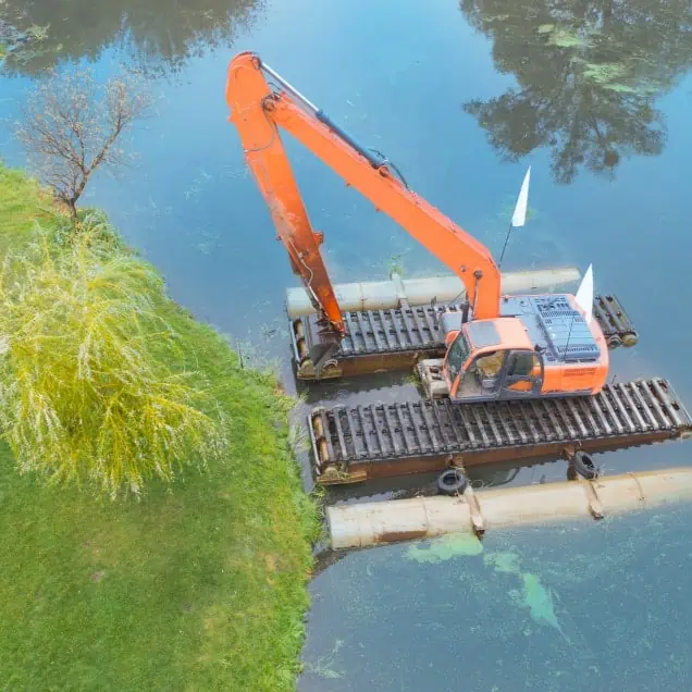 An aerial view of an orange excavator repairing a lake.