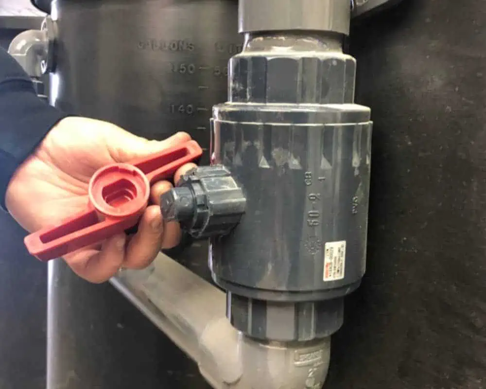 A person is holding a red handle on a water valve.