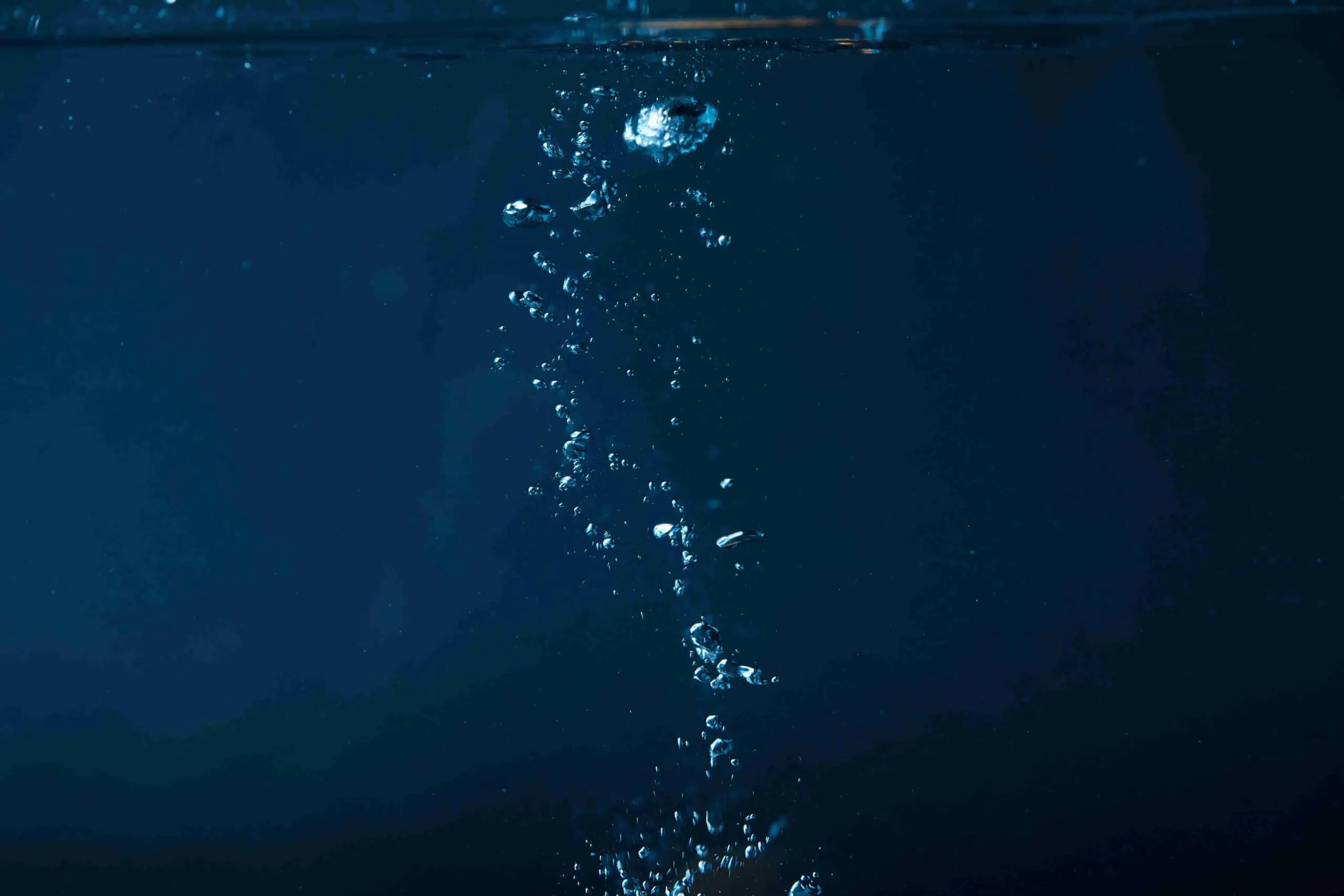 Bubbles rising in dark blue water against a deep blue background, reflecting pristine water quality.